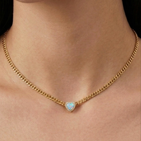 A close-up of a model's neck wearing a gold chain necklace with a small heart-shaped light blue stone pendant.