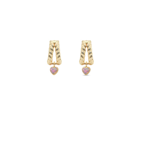A pair of gold huggie hoop earrings with textured vertical bars and a small dangling pink heart charm, shown on a plain white background.