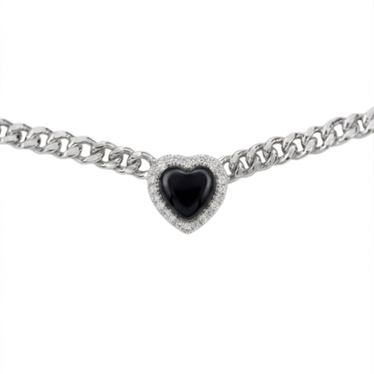 A silver-toned curb chain bracelet featuring a heart-shaped centerpiece with a glossy black center stone surrounded by a halo of small clear stones, shown against a plain white background.