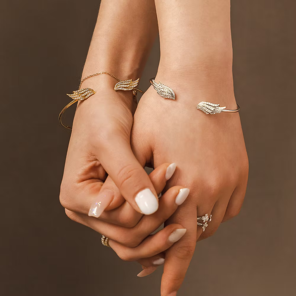 BLOOMTINE | Statement Premium Angel Wing Bangle in Silver and Gold. Two hands holding each other with angel wing. Shown as the perfect gift idea
