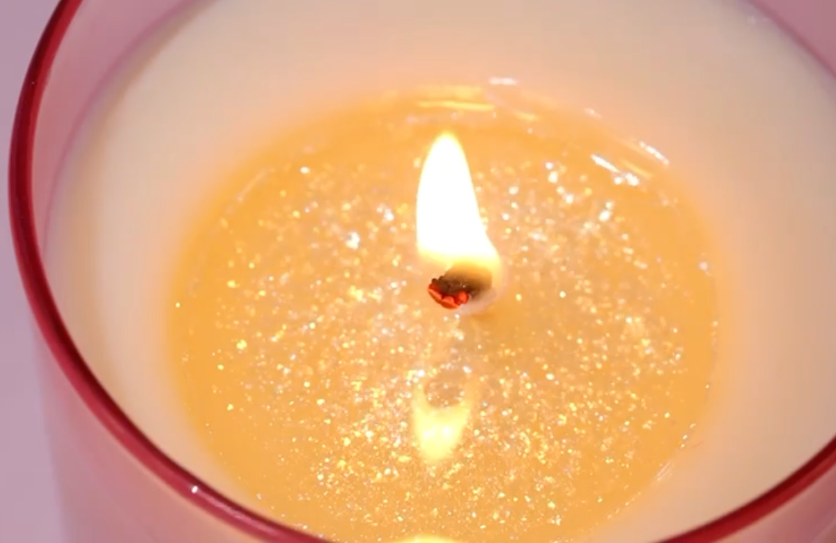 Candle in a glass container with a small flame. Handcrafted in London, the BLOOMTINE Glitter Bomb™ soy wax candle features a creamy citrus and vanilla sugar fragrance. This eco-friendly, tarnish-free pink glass candle offers a 40-50 hour burn time and an innovative iridescent glitter-infused melt pool