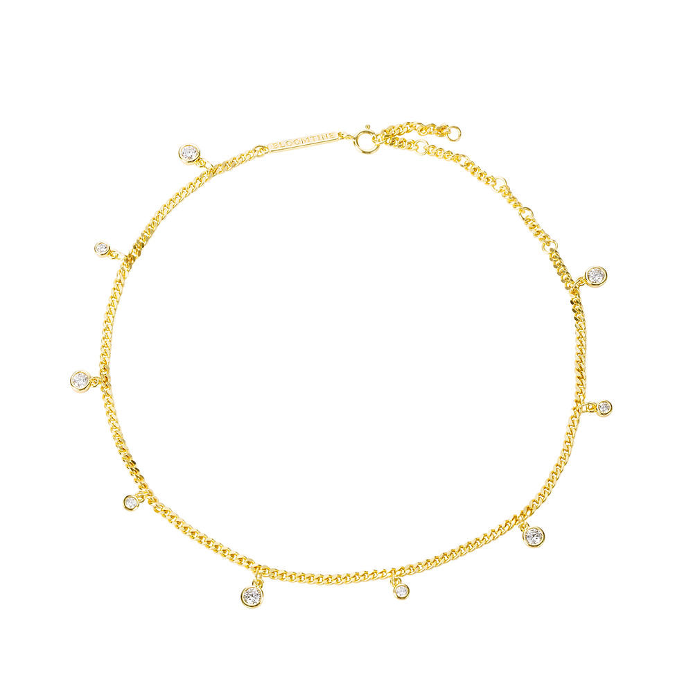 A close-up shot of the Illuminess™ Apah Water Goddess Anklet in premium gold vermeil, modeled on an olive-toned ankle. The dainty silver chain features shimmering lab-diamond droplets that catch the light, creating a liquid-sparkle effect