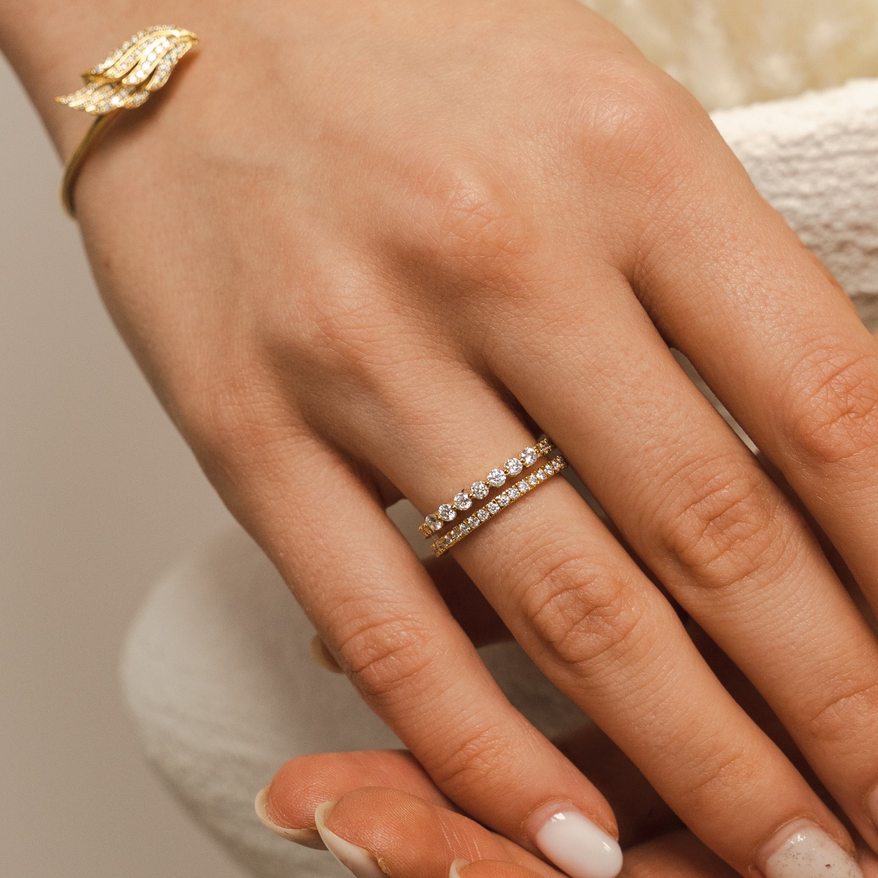 Close-up of a hand wearing two gold rings with a neutral background. The BLOOMTINE Illuminess™ Sterling Silver Combi Ring featuring a fused pavé and bezel-set design. This two-in-one moissanite stack is handcrafted in solid sterling silver with a white rhodium finish, offering the look of a curated ring stack with the comfort of a single band.