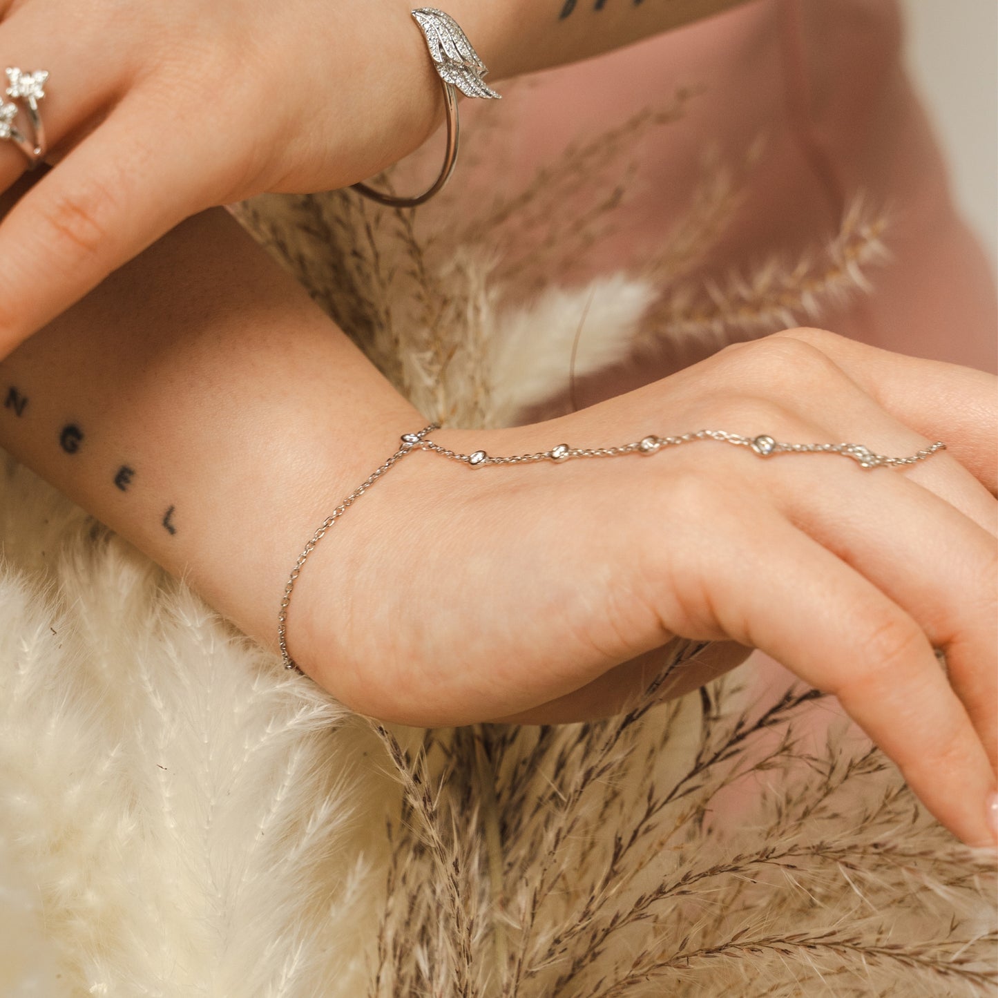 Close-up of a hand wearing a delicate bracelet with a soft background. Adjustable sterling silver hand chain by BLOOMTINE with 6 lab-grown diamonds. Known as a finger chain or hand harness, this tarnish-resistant rhodium-plated piece features a diamond-cut chain for maximum sparkle, fitting wrist sizes 5.75 to 7.5 inches