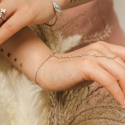 Close-up of a hand wearing a delicate bracelet with a soft background. Adjustable sterling silver hand chain by BLOOMTINE with 6 lab-grown diamonds. Known as a finger chain or hand harness, this tarnish-resistant rhodium-plated piece features a diamond-cut chain for maximum sparkle, fitting wrist sizes 5.75 to 7.5 inches