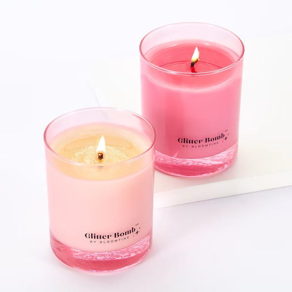 Two-pink-Glitter-Bomb-branded-candles. A professional-product-shot of a pair-of-luxury-scented-candles with visible-burning-flames shown-on-a-clean-white-background. These-vibrant-pink-candles feature the-signature-Glitter-Bomb-logo and are designed-as-a-premium-home-fragrance-gift-set. The-image-highlights the-glowing-wicks and sleek-glass-vessel-design, perfect-for-Valentine-gifting, birthdays-or-creating-a-romantic-atmosphere.