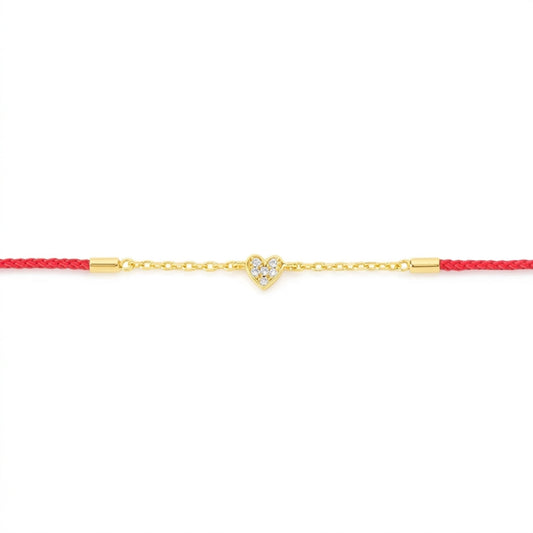 A delicate gold chain bracelet featuring a small heart-shaped charm paved with clear stones, suspended on a vibrant red cord with gold end caps, set against a plain white background.