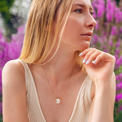 Bloomtine-Loves-Frequency-necklace-lifestyle. A professional-lifestyle-shot of a woman-wearing-the-signature-gold-heartbeat-pendant-necklace against a backdrop-of-soft-purple-flowers. This-18kt-gold-vermeil-jewellery features a unique-heartbeat-frequency-design, symbolizing-connection-and-love. The-natural-lighting highlights the-polished-finish, while the-floral-setting-emphasizes the-romantic-botanical-aesthetic of the Bloomtine-brand. An-ideal-meaningful-gift for anniversaries-or-special-occasions, show